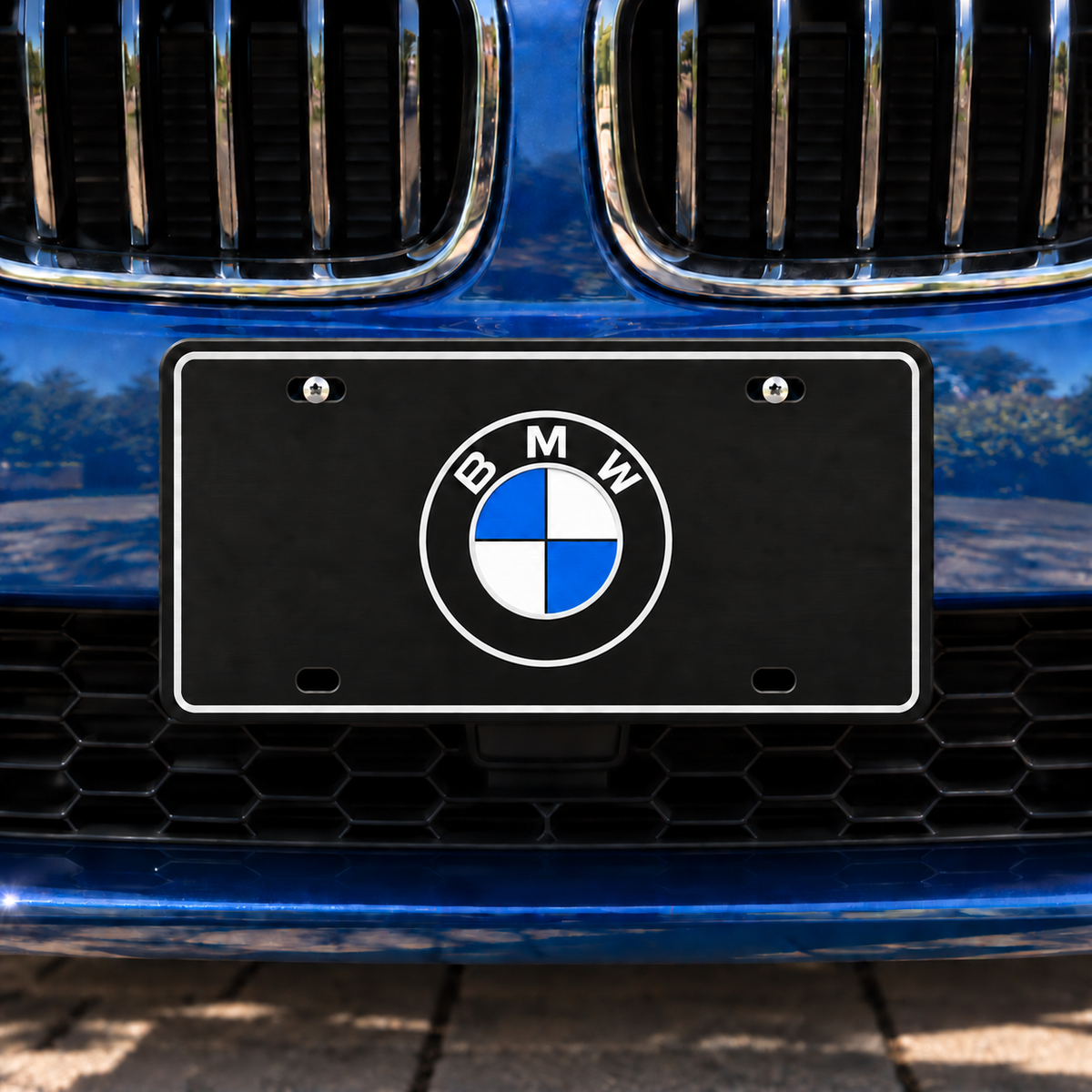 Lifestyle illustration of the black BMW decorative tag with silver border and blue-and-white roundel mounted on the front of a blue vehicle.